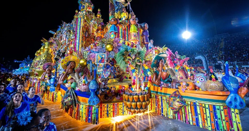 A glittering Carnival float lit in blue, gold and pink on the Sambódromo avenue at night
